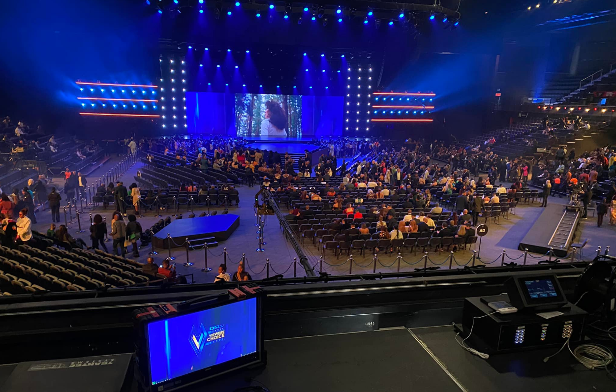 DStv Mzansi Viewers' Choice Awards 2022 — SunBet Arena auditorium view from FOH camera position, blue-lit stage with overhead truss