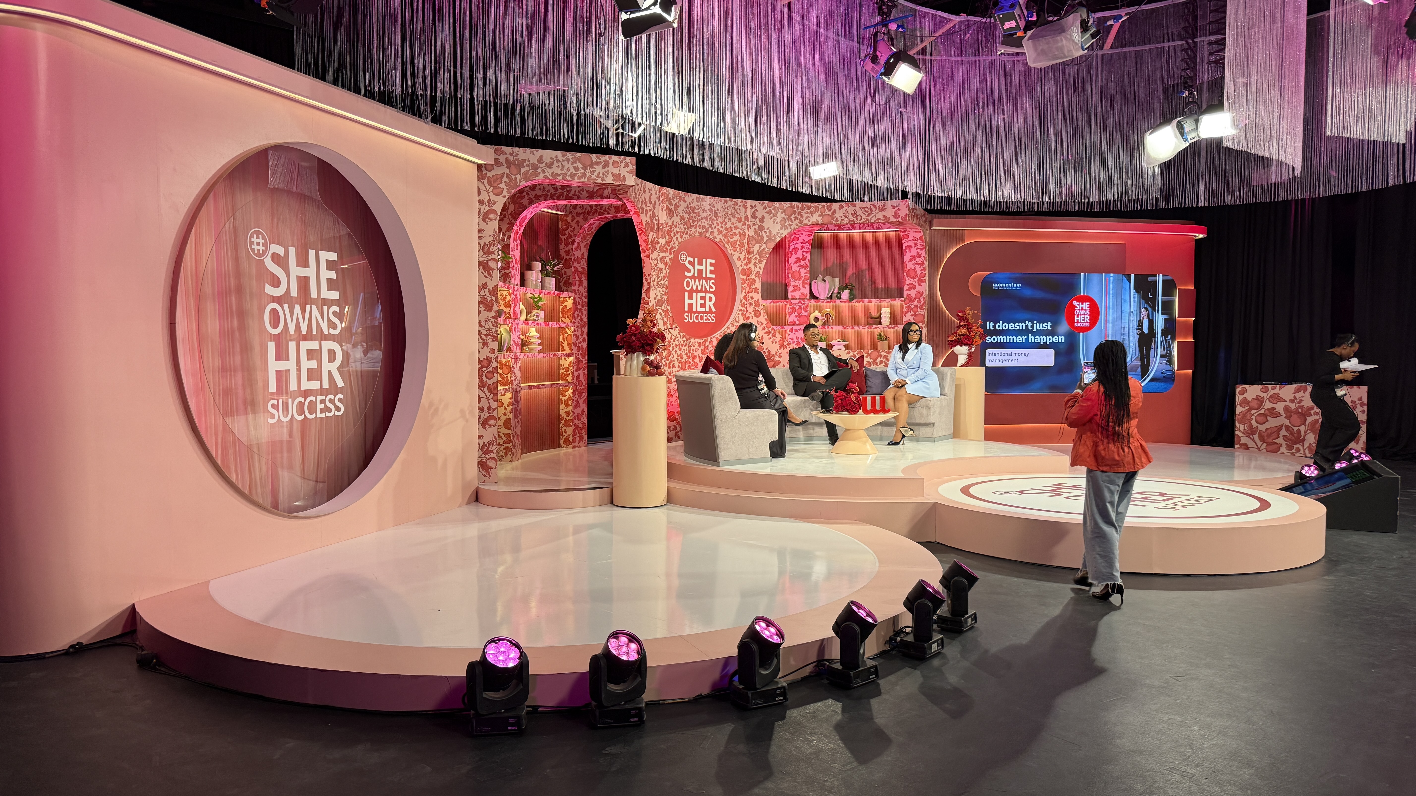 She Owns Her Success — Momentum studio talk-show set with pink floral motif and circular signage