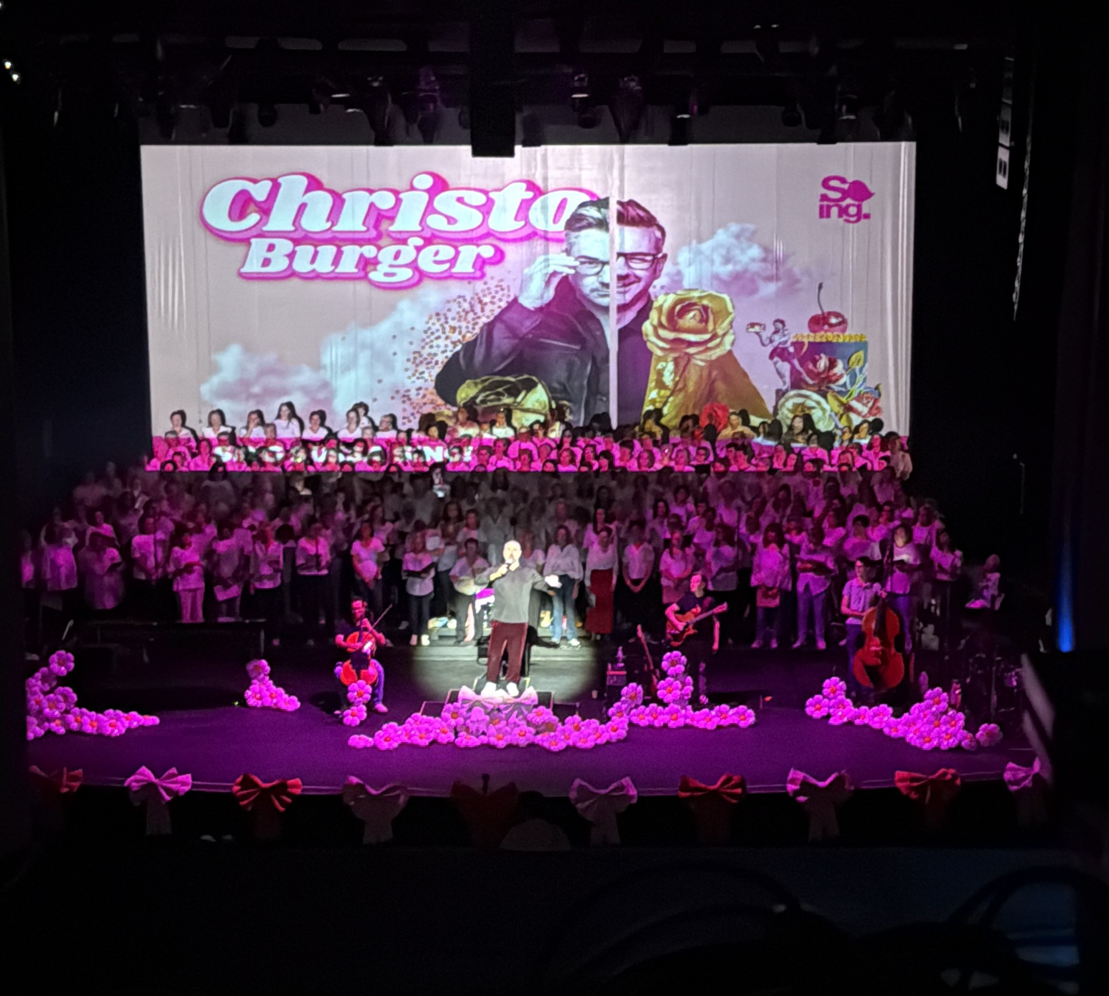 Sing Sussa Sing — Christo Burger theatre production with pink-wash stage and floral set dressing